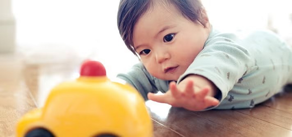 Niemowlę leżące na brzuszku sięga po żółtą zabawkę Niemowlę leżące na brzuszku sięga po żółtą zabawkę