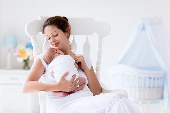 Czas połogu po cesarce mama wypoczywająca w fotelu i przytulająca śpiące maleństwo Czas połogu po cesarce mama wypoczywająca w fotelu i przytulająca śpiące maleństwo