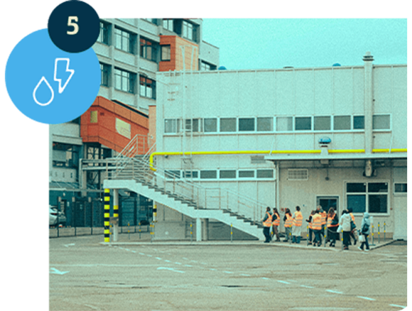 Ludzie w kamizelkach odblaskowych przed budynkiem przemysłowym.